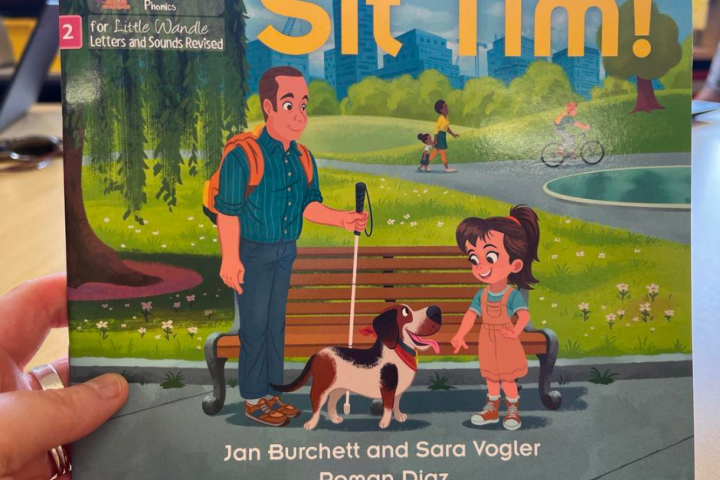 he image shows the cover of a children's book titled "Sit Tim!" from the Collins Big Cat series. The cover features a colorful illustration set in a park. On the left, there is a man with dark hair, wearing a blue shirt, green suspenders, and blue pants. He is holding a white cane, indicating that he is vision impaired. Next to him is a small brown and white dog with a happy expression. On the right, a young girl with ponytailed brown hair, wearing an orange jumpsuit and light blue shirt, is smiling and looking at the dog. In the background, there are scenes of a park with trees, a pond, and people walking and cycling. The authors' names, Jan Burchett and Sara Vogler, along with the illustrator's name, Roman Diaz, are mentioned at the bottom of the cover.