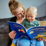 A mother sits with her young child reading a children’s book]